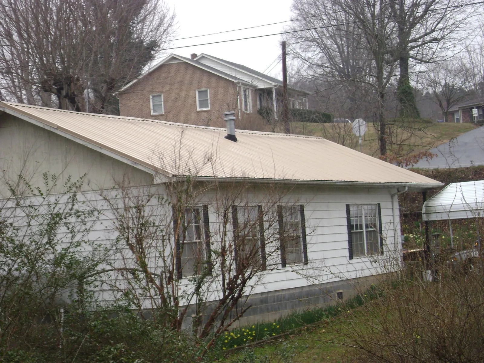 Tan metal roof on a white sided house set into a hillside — Commercial Roofing by Roofing Brothers in Corinth